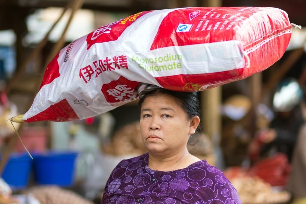 A woman carrying a large monosodium glutamate bag on her head in the street of Mandalay, Myanmar