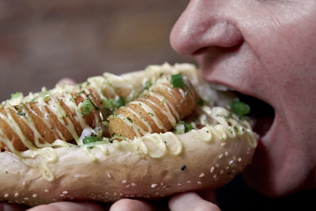 A woman bites into a Japan’s Darling hotdog, which combines fried potato croquettes, roasted onions, Japanese mayonnaise, teriyaki sauce, chives and nori flakes. PHOTO: Corbis