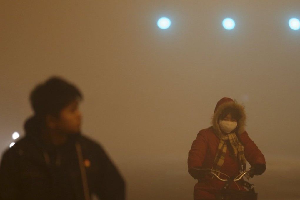 A woman wears a mask while riding a bicycle along a Beijing street shrouded in heavy smog and thick fog on Wednesday morning. Photo: Reuters