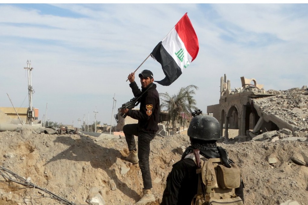 A member from the Iraqi security forces holds an Iraqi flag aloft in the city of Ramadi on Sunday, amid the routing of Islamic State forces there. Photo: Reuters ,