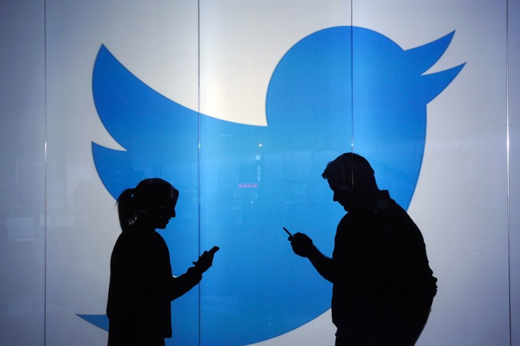 People are seen as silhouettes as they check mobile devices whilst standing against an illuminated wall bearing Twitter Inc's logo in London. Photo: Reuters