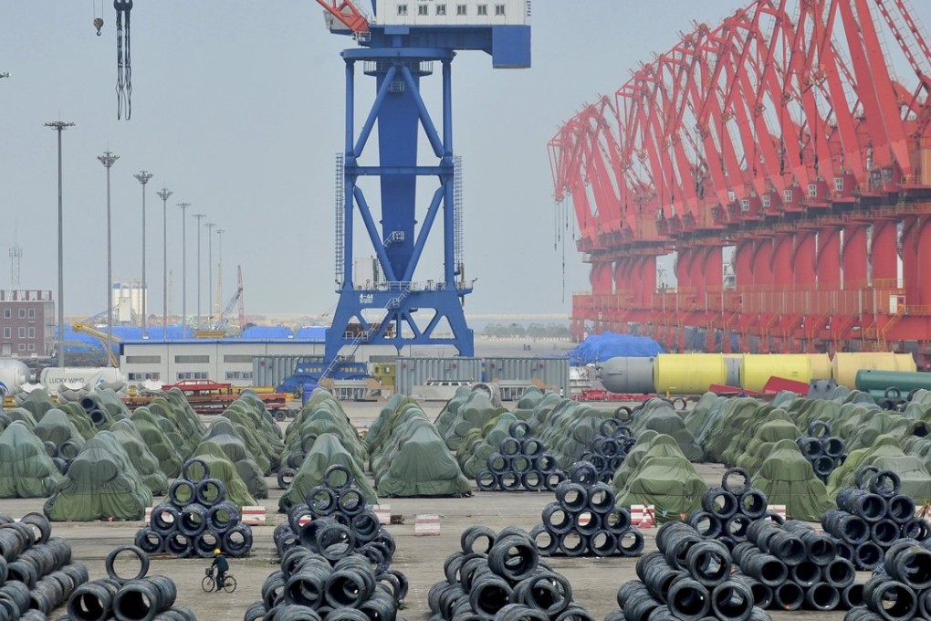 A worker rides his bicycle past piles of steel coils for export at a port in Yingkou, Liaoning province. Photo: Reuters