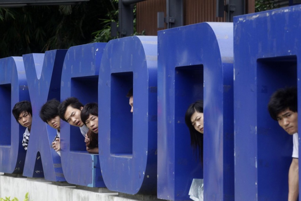 Workers look on from a Foxconn logo near the gate of a Foxconn factory in the township of Longhua, Guangdong province. The once controversial firm is back in favour with job seekers who are faced with a toughening market. Photo: Reuters