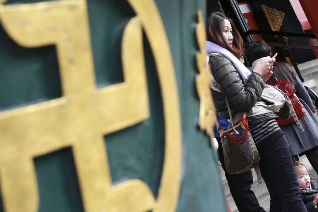 Visitors to Tokyo stand next to a religious ornament with the manji symbol. Photo: AP