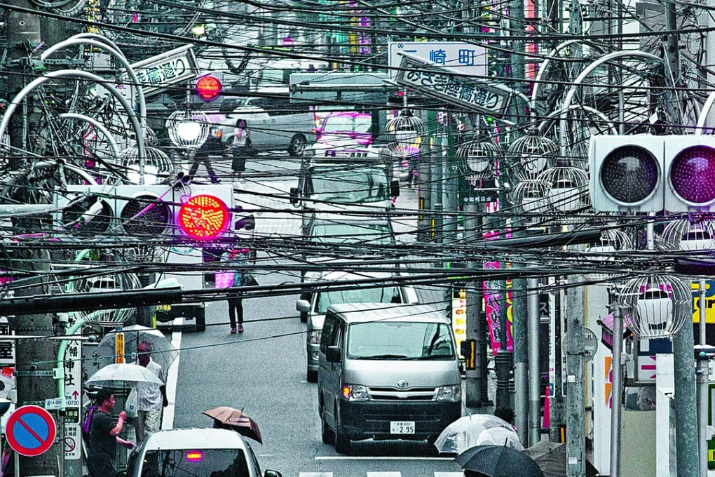 Power and utility cables hang from poles alongside a shopping strip in Tokyo. Photo: Bloomberg
