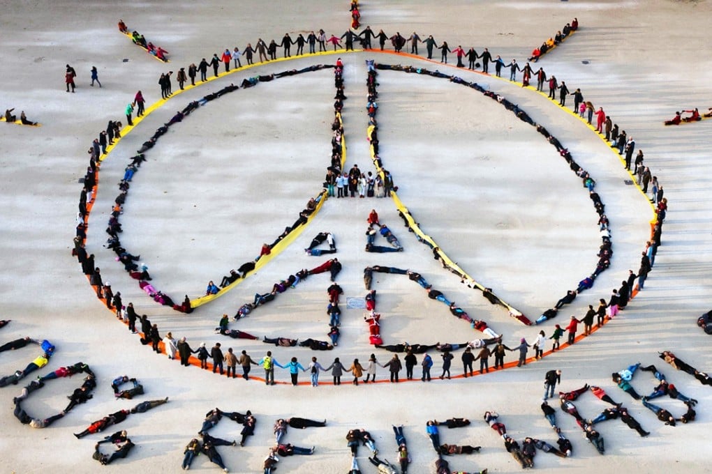 People make the “Pray for Paris” sign along with the slogan “100 per cent renewable” near the Eiffel Tower in Paris on the sidelines of the COP21 climate change conference. Photo: AFP