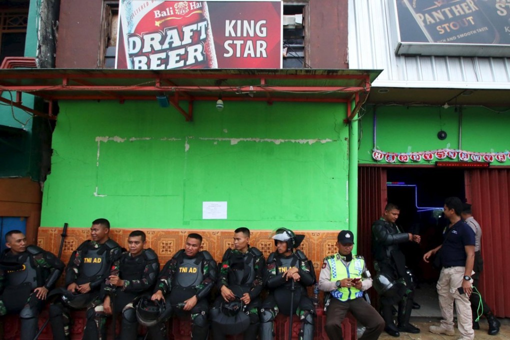 Indonesian soldiers and policeman sit and guard in front of a cafe building at Kalijodo red-light district in Jakarta, Indonesia. Photo: Reuters