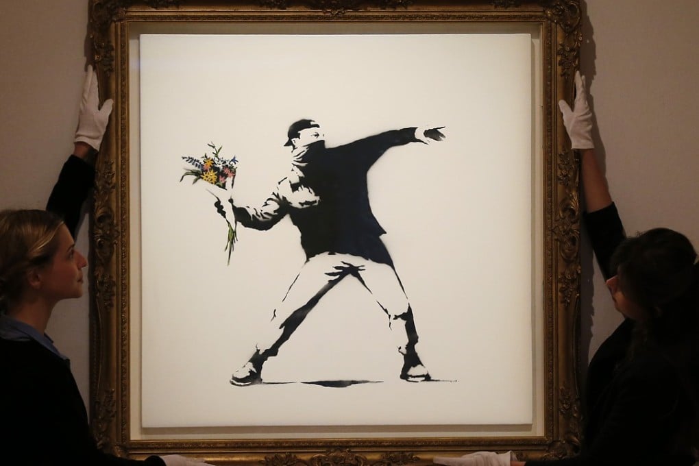 Bonhams employees adjust a spray paint work by urban artist Banksy at Bonhams auction house in London. Photo: AP
