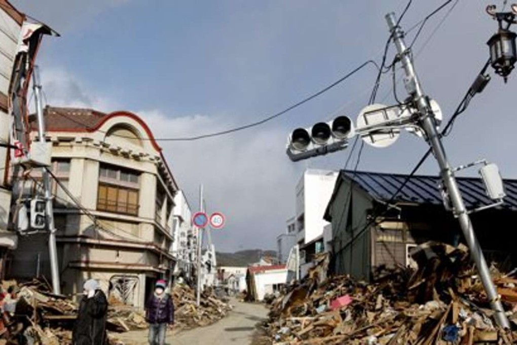 Tsunami survivors walking in a devastated street with debris piled up on the sidewalk in Kesennuma, Miyagi Prefecture, northeastern Japan. Photo: EPA