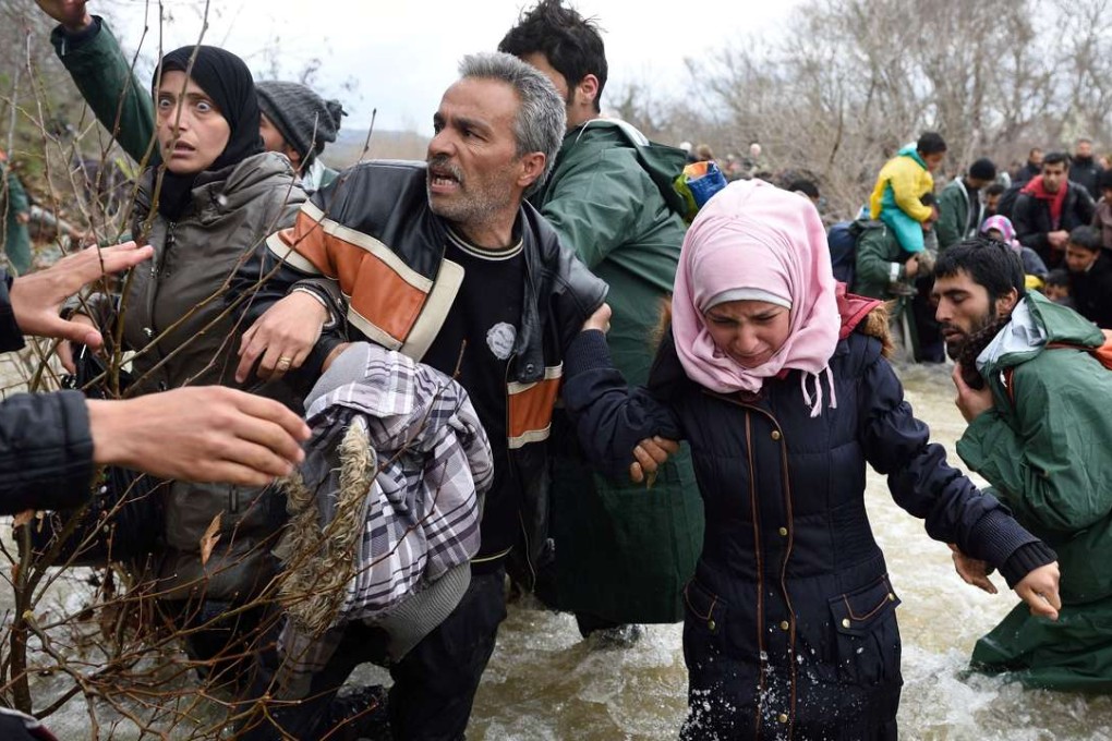 Refugees and migrants try cross a river on their way to Macedonia from a makeshift camp at the Greek-Macedonian border on Monday. Photo: AFP