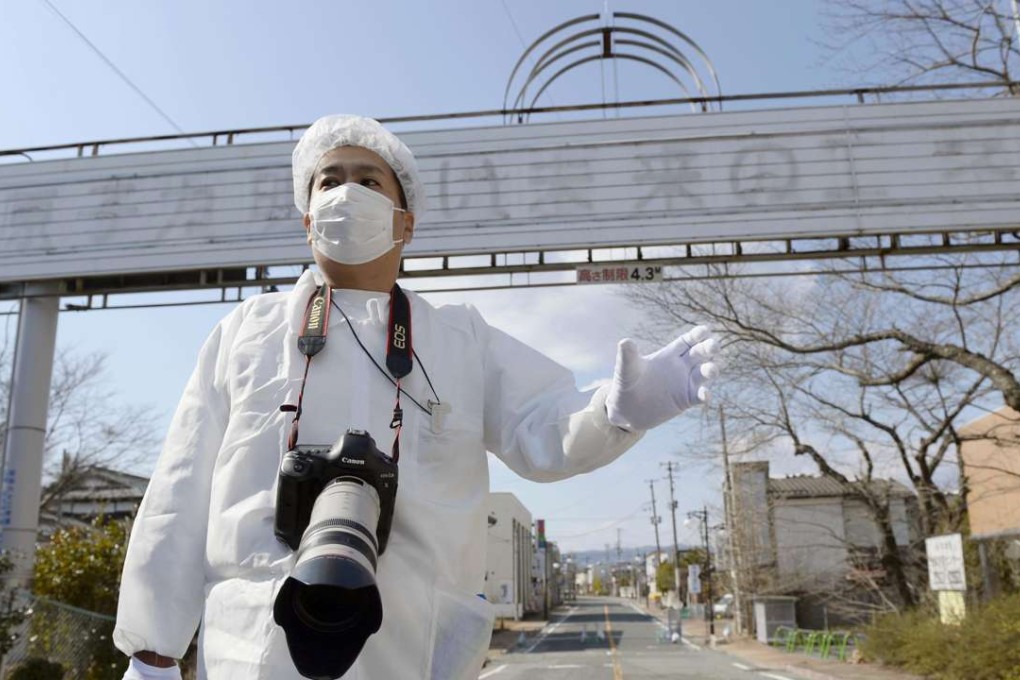 A worker stands in front of a sign which used to read “Nuclear power: the energy for a bright future” in Fukushima. Photo: Kyodo