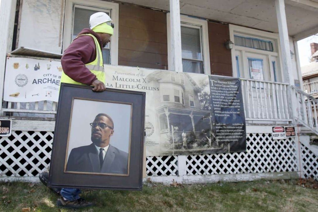 Rodnell P. Collins carries a painting of Malcolm X outside the house where the slain African-American activist spent part of his teen years, Tuesday, March 29, 2016, in the Roxbury section of Boston. Archeologists are undertaking a two-week dig at the home in an effort to uncover more about his early life, when he was known as Malcolm Little and lived there with his sister's family in the 1940s. (AP Photo/Bill Sikes)