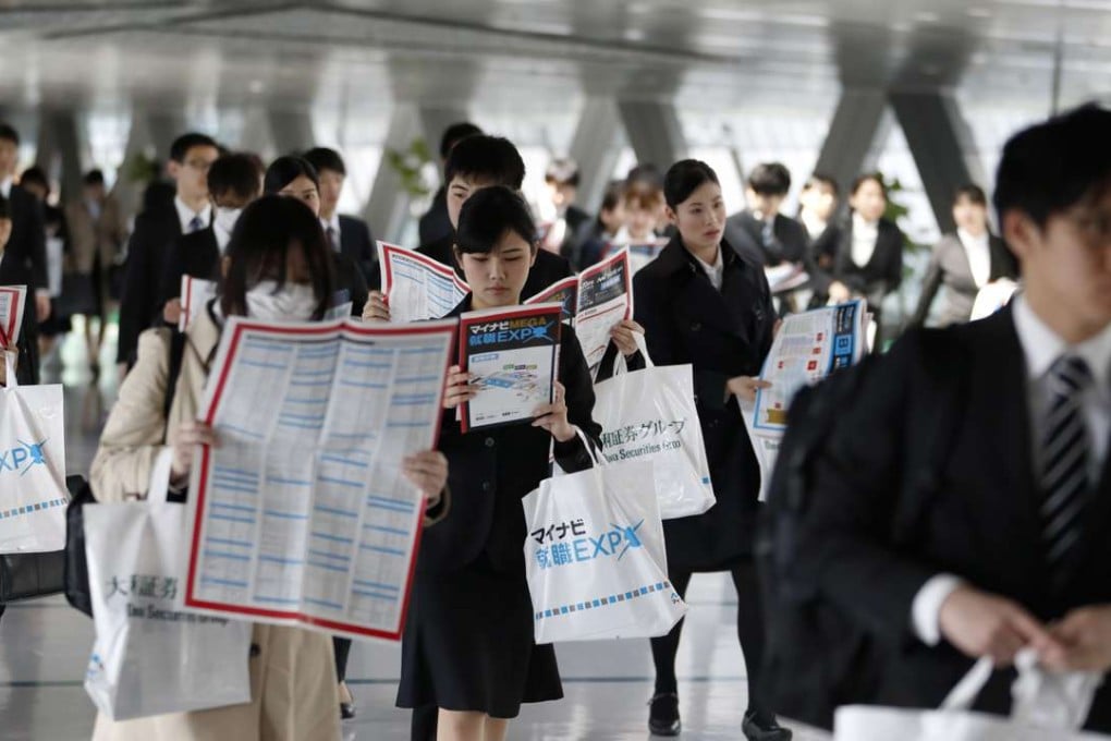 University students hold floor maps as they walk through a job fair in Tokyo. Many younger workers in Japan accept taking non-regular contract jobs with longer hours due to their lack of experience. Photo. Bloomberg