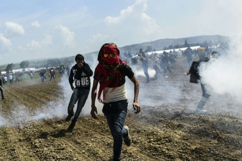 Refugees and migrants flee tear gas as they clash with Macedonian police during a protest to reopen the border near their makeshift camp in the northern Greek border village of Idomeni on Sunday. Photo: AFP