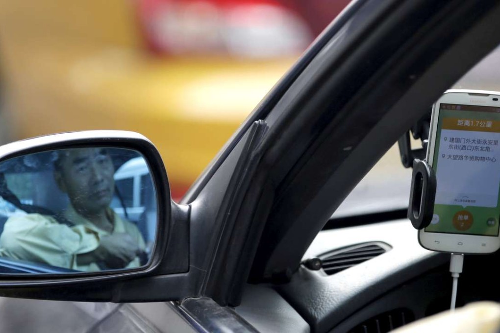 A taxi driver is reflected in a side mirror as he uses the Didi Chuxing car-hailing application in Beijing. Photo: Reuters