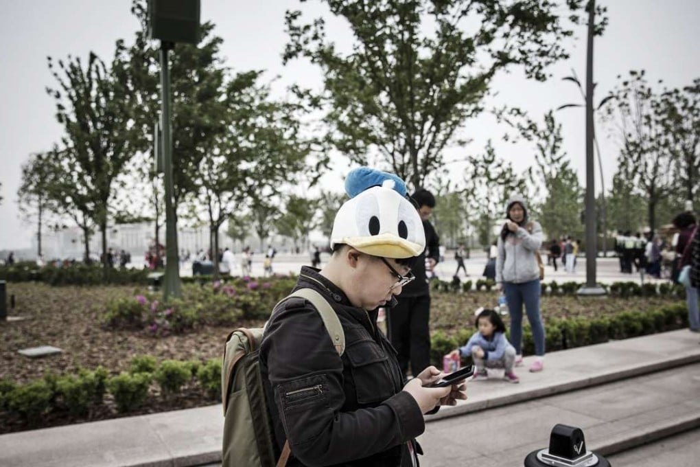 A visitor wearing a Donald Duck hat uses a smartphone at the Disneytown retail area of Walt Disney Co.'s Disneyland Resort in Shanghai, China, on May 7, 2016. Photo: Bloomberg
