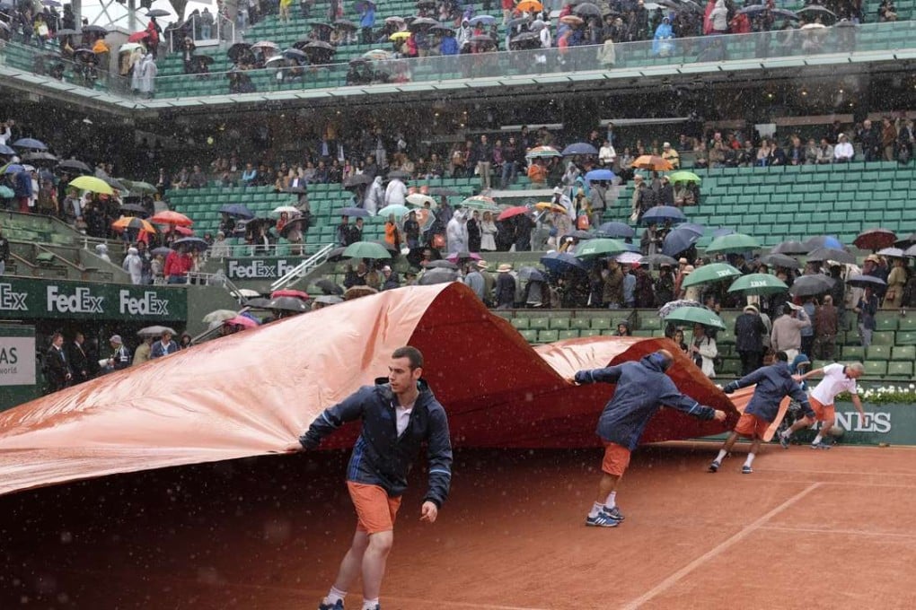 Stadium workers cover the clay court as rain pelts down. Photo: AP