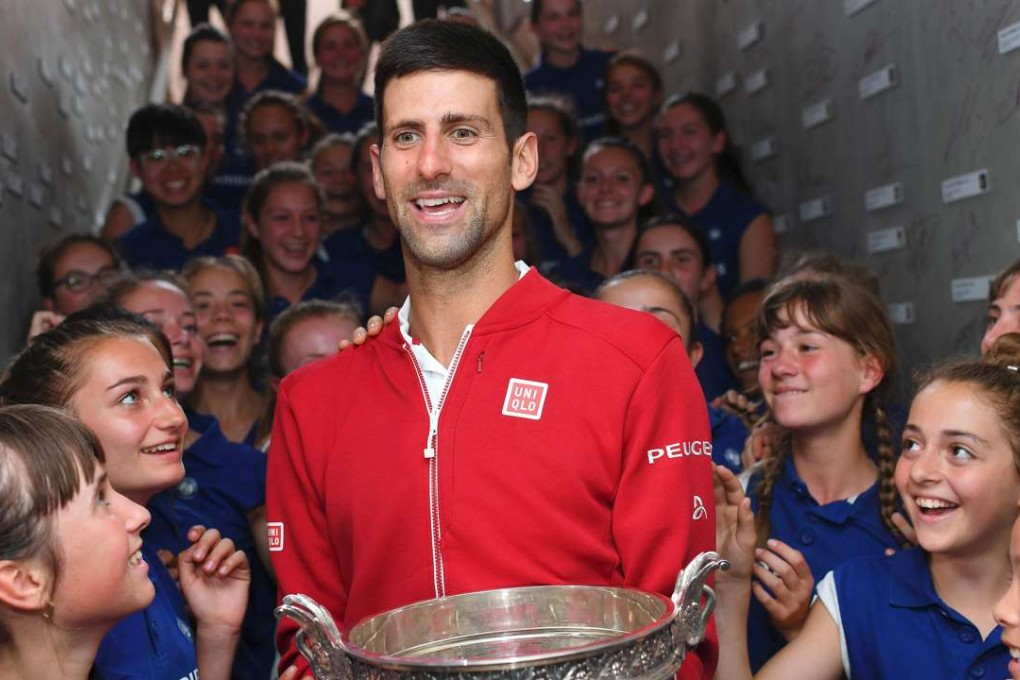 Novak Djokovic poses with his trophy flanked by ball girls. Photo: AFP