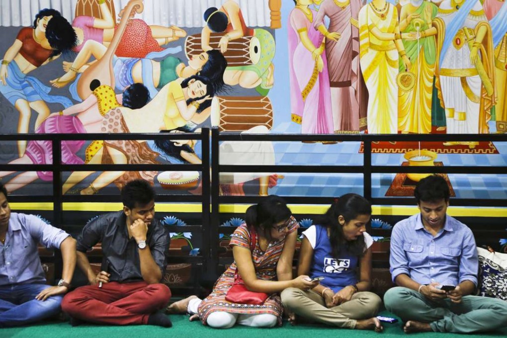 Young Buddhist devotees use their mobile phones as they sit under the frescos for prayer inside a temple during Buddha Purnima in Kolkata, India on May 21, 2016. Photo: AP