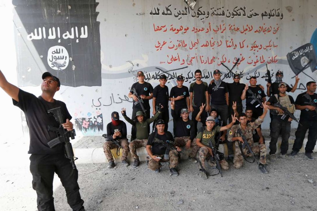 An Iraqi counterterrorism soldier poses for a selfie with comrades against the backdrop of an Islamic State propaganda mural in Fallujah on Sunday. Photo: Reuters