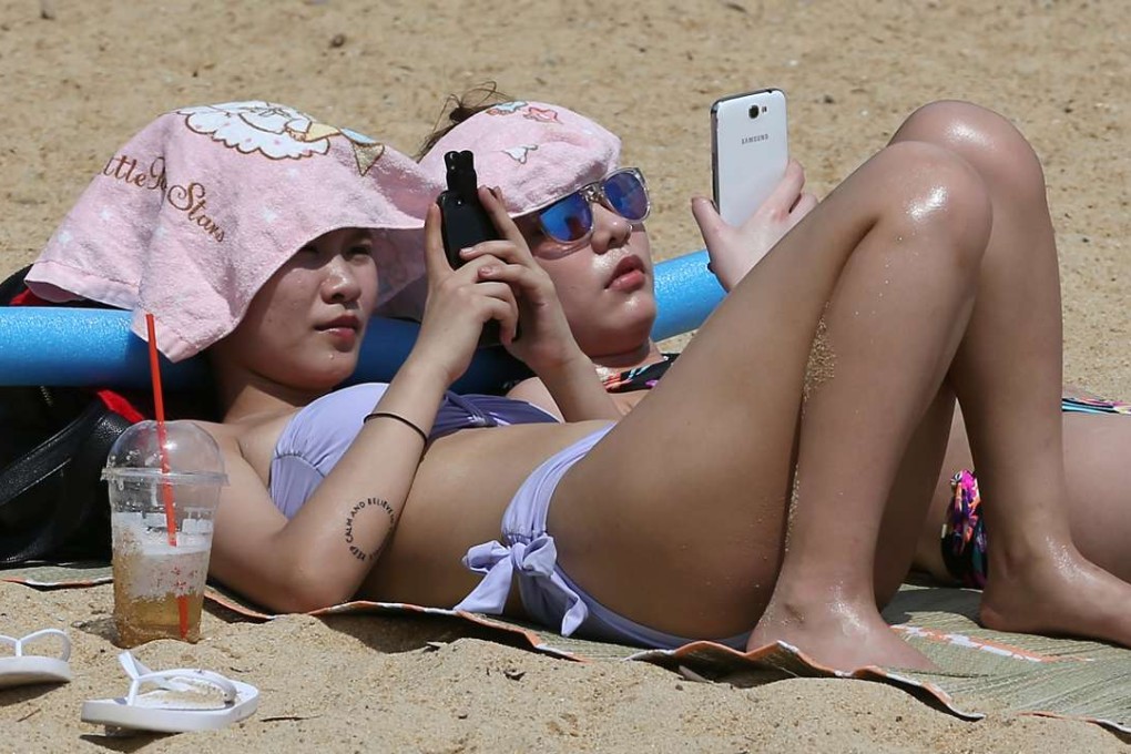 Why not both? Sunbathers work on their tan while using their mobile devices. Photo: Nora Tam