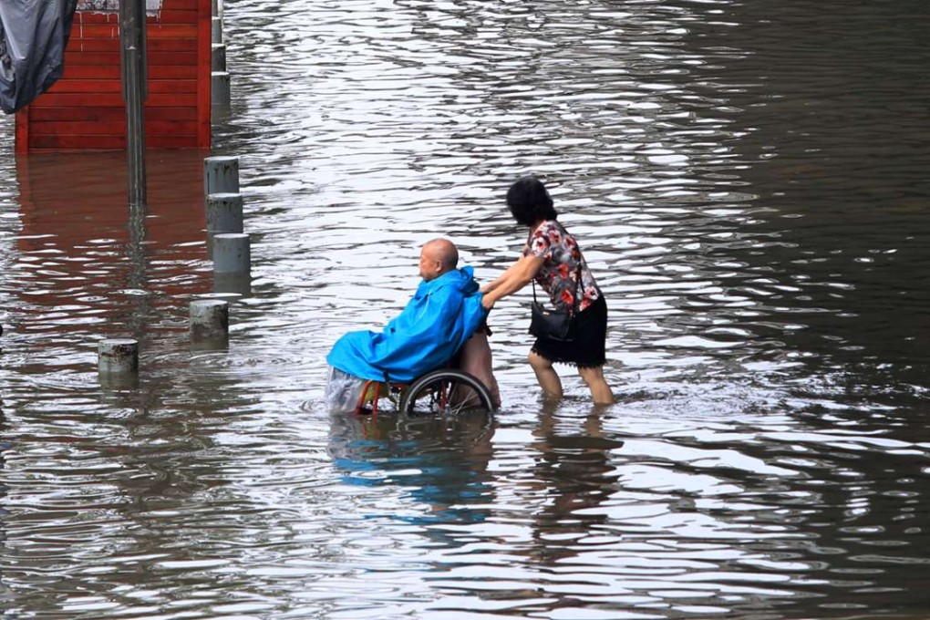 A woman pushes an old man in an wheelchair across a flooded Wuhan street on Wednesday. Photo: Simon Song