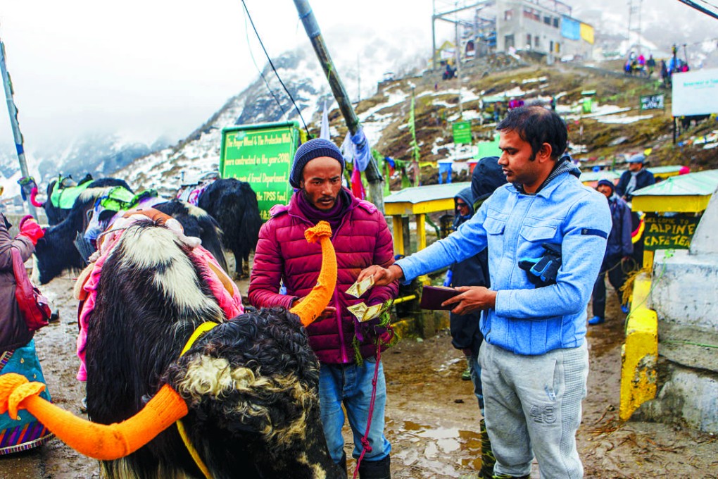 A tourist (right) hands over Indian rupee banknotes to a vendor standing next to a cow at Tsongmo Lake near the Nathula Pass. Photo: Bloomberg