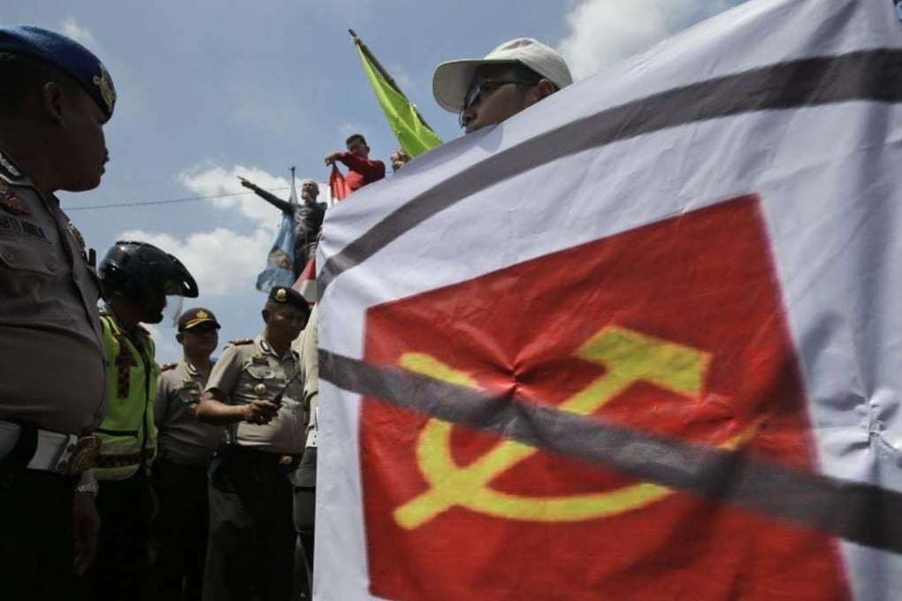 A man carries a banner of defaced communist symbol during a protest against the discussion of anti-communist massacres in 1965-66 outside the venue of the event in Jakarta, Indonesia, Monday, April 18, 2016. Photo: AP
