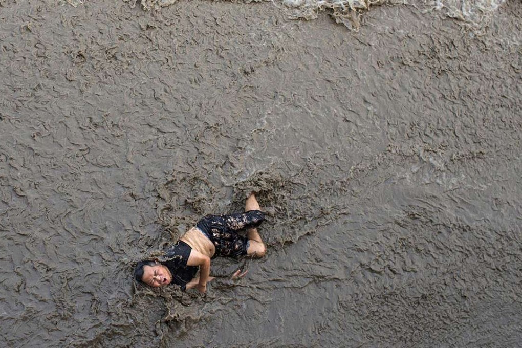 An injured man lies on the edge of the Qiantang River as the water rapidly rises. Photo: SCMP Pictures