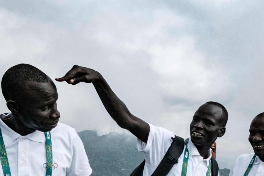 South Sudan's athlete Yiech Pur Biel (C) and James Nyang Chiengjiek (L) based in Kenya for the Refugee Olympic Team (ROT) joke during a visit to the statue of Christ the Redeemer ahead of Rio 2016 Olympic games atop Corcovad Hill in Rio de Janeiro, Brazil, on July 30, 2016. The International Olympic Committee (IOC) selects 10 refugee athletes to set a refugee's team for the first time, to bring about hope to people displaced by conflicts or war in the world. / AFP PHOTO / YASUYOSHI CHIBA