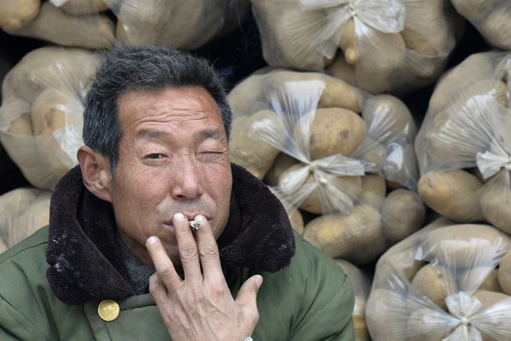 A vendor smokes a cigarette in front of sacks of potatoes piled up on a truck at a market in Shanxi province. Photo: Reuters
