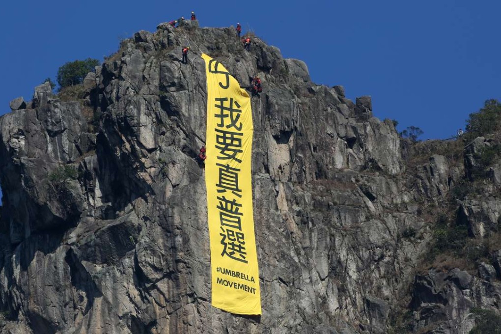 Workers take down a banner demanding “genuine universal suffrage” from atop Lion Rock. Photo: Nora Tam