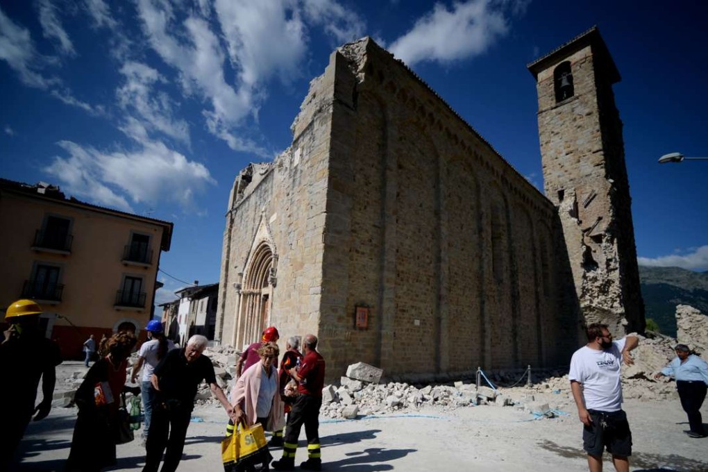 People walk past an earthquake damaged church during search and rescue operations in Amatrice. Photo: AFP