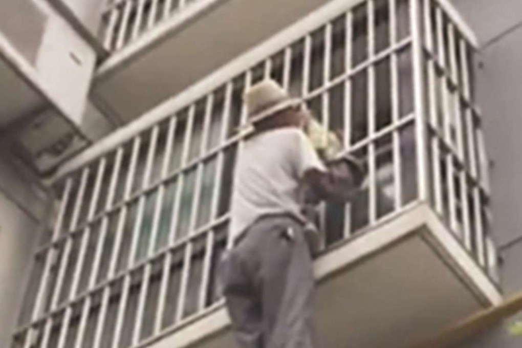 A Chinese worker holds on to the four-year-old boy, who was left hanging in railings after climbing over a second-floor balcony after being left home alone. Photo: SCMP Pictures