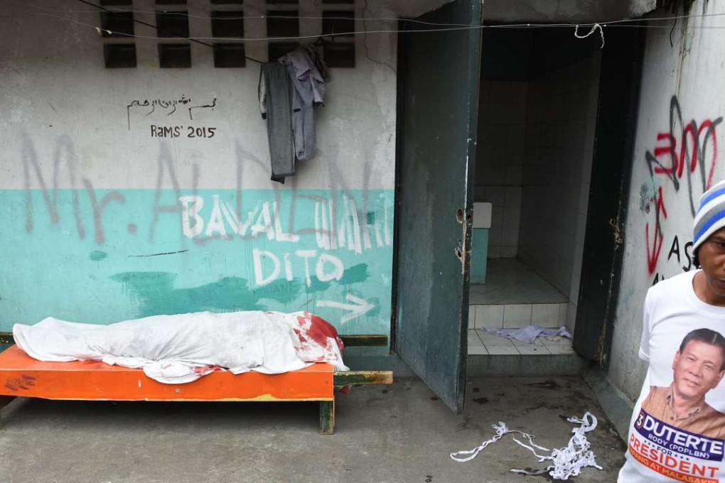 A man wearing T-shirt featuring President Rodrigo Duterte, stands next to the sheet-covered body of a man killed during a police anti-drug operation in Manila City. Photo: AFP