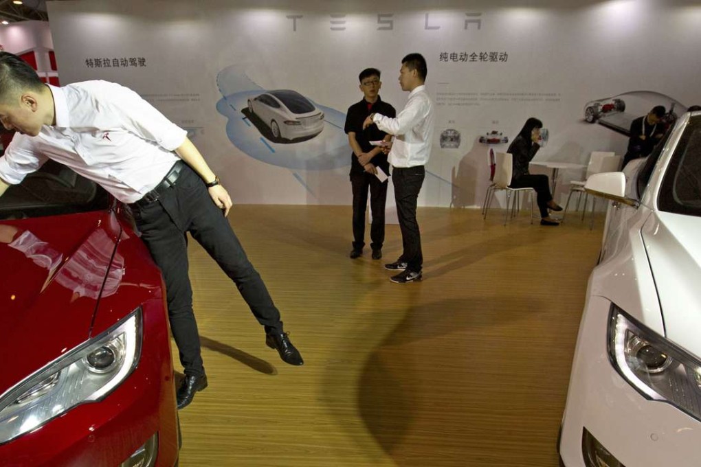 A staff member cleans the hood of a Tesla Model S electric car near a display advertising Tesla's self-driving features at the Beijing International Automotive Exhibition in Beijing, China. Photo: AP