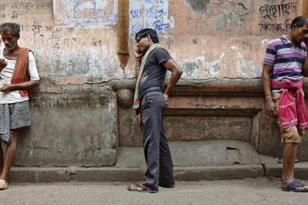 Labourers speak on mobile phones opposite a public call office (PCO) in a market area in Kolkata, India. Photo: Rupak De Chowdhuri/Reuters