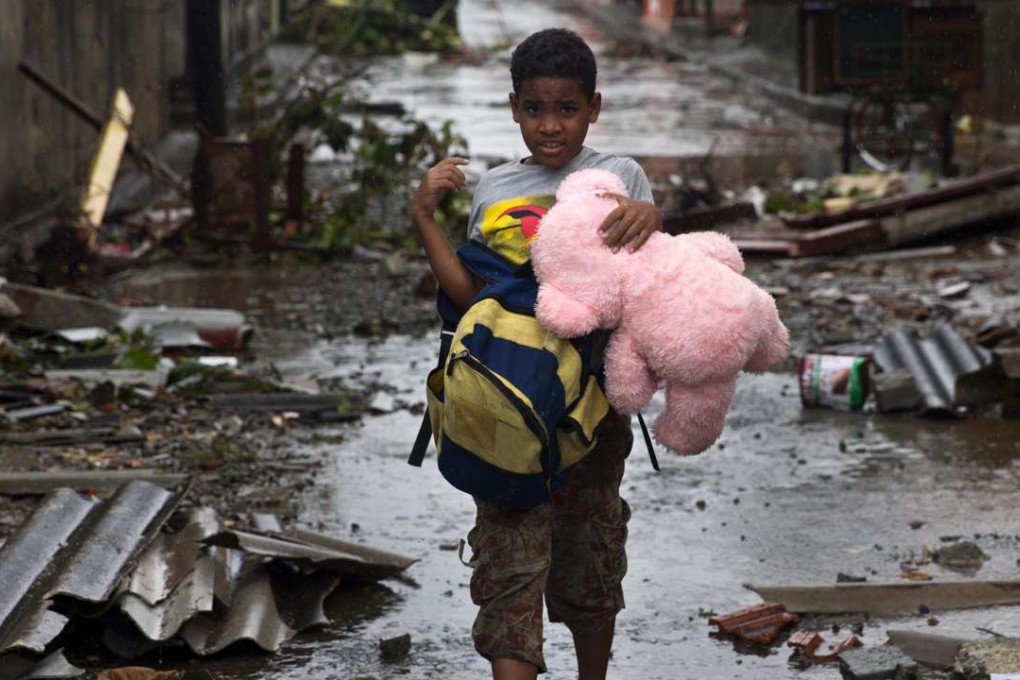 A boy walks, carrying a backpack and a teddy bear, through a street littered with debris the morning after Hurricane Matthew drove across Baracoa, Cuba. Photo: AP