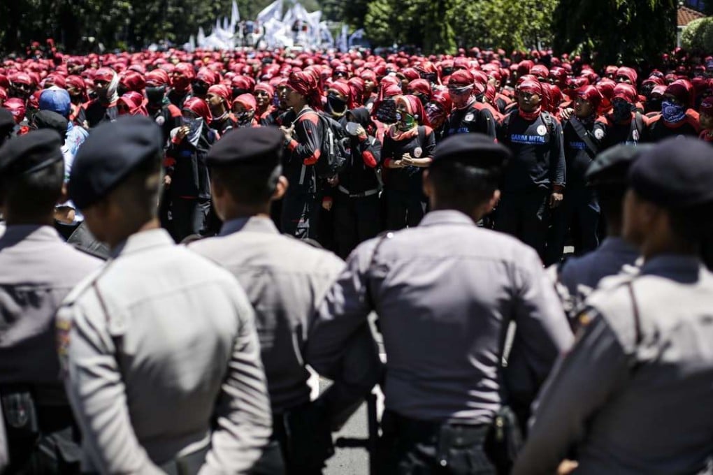 Indonesian labourers protest against the government’s tax amnesty and demand better wages as police officers stand guard during a rally in Jakarta last month. Photo: EPA