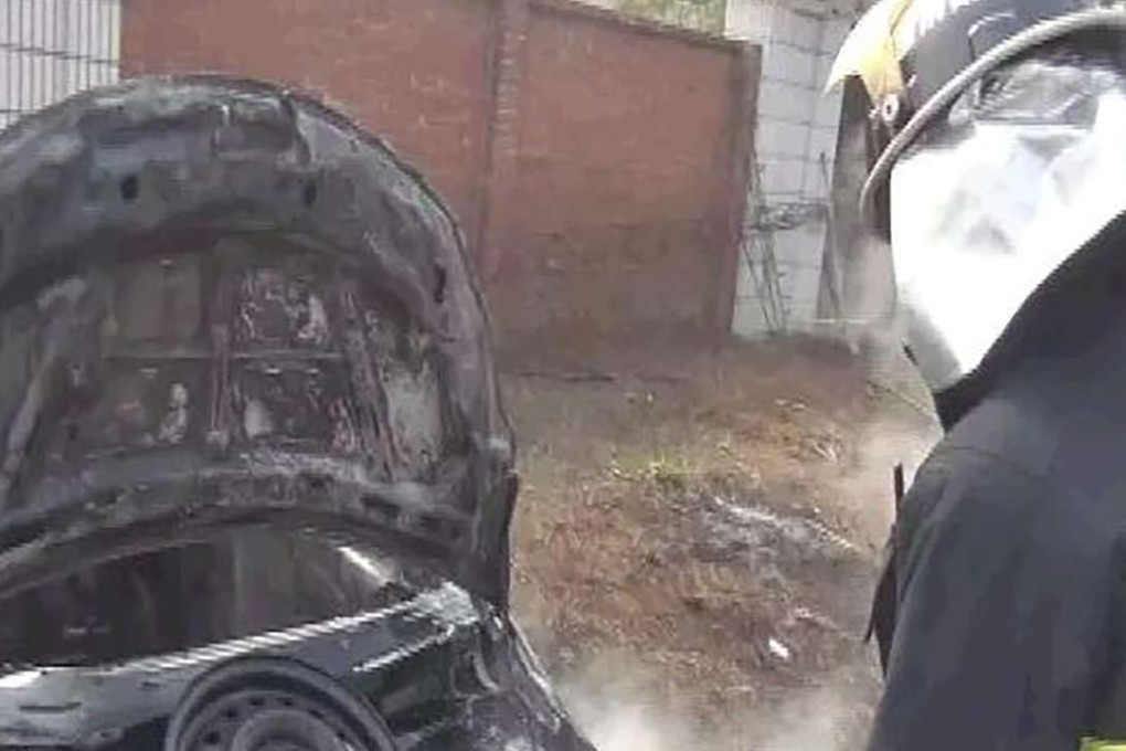 A firefighter wets down the smouldering remains of the car. Photo: SCMP Pictures