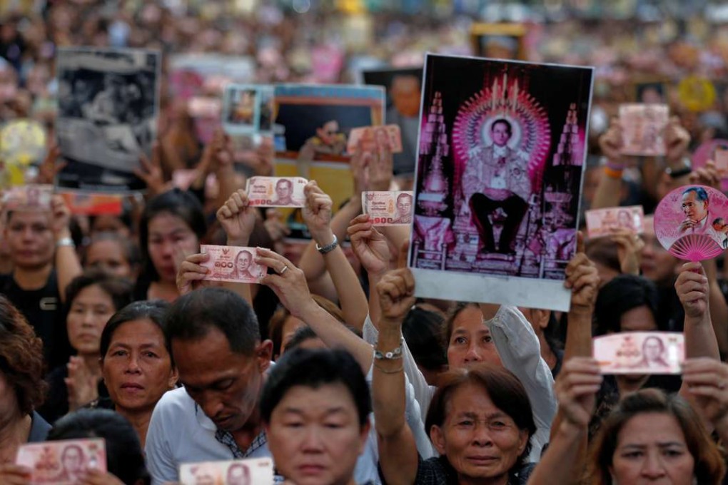 People hold Thai baht notes and portraits of Thailand's late King Bhumibol Adulyadej as they wait on the roadside while his body is moved from Siriraj hospital, where he died, to the Grand Palace, in Bangkok, Thailand. Photo: Reuters