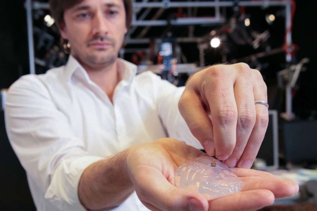 Grégoire Courtine holds a silicon model of a primate's brain and a brain implant. The brain-spine interface uses a microelectrode like this one to detect spiking activity of the brain's motor cortex. Photo: Alain Herzog/EPFL.