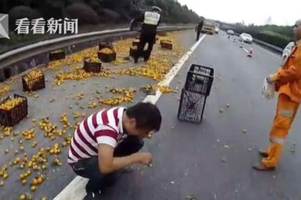 The Chinese truck driver (left) squats beside the road as he weeps as police and other emergency workers help to clear the road of oranges after the accident. Photo: SCMP Pictures