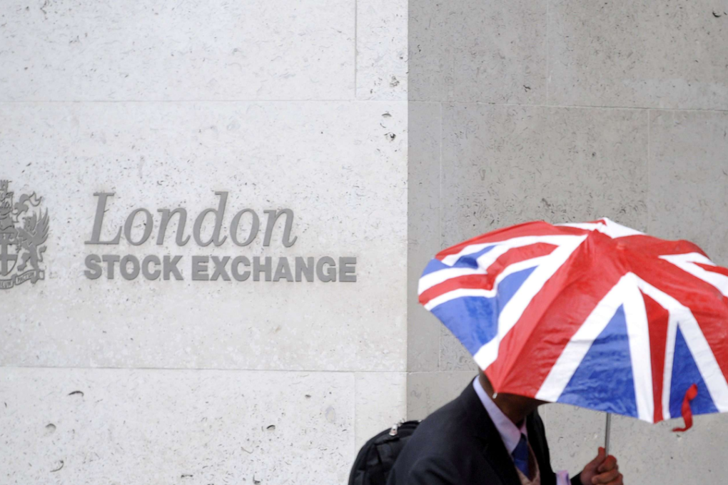 A worker shelters from the rain as he passes the London Stock Exchange in the City of London. Photo: REUTERS/TOBY MELVILLE