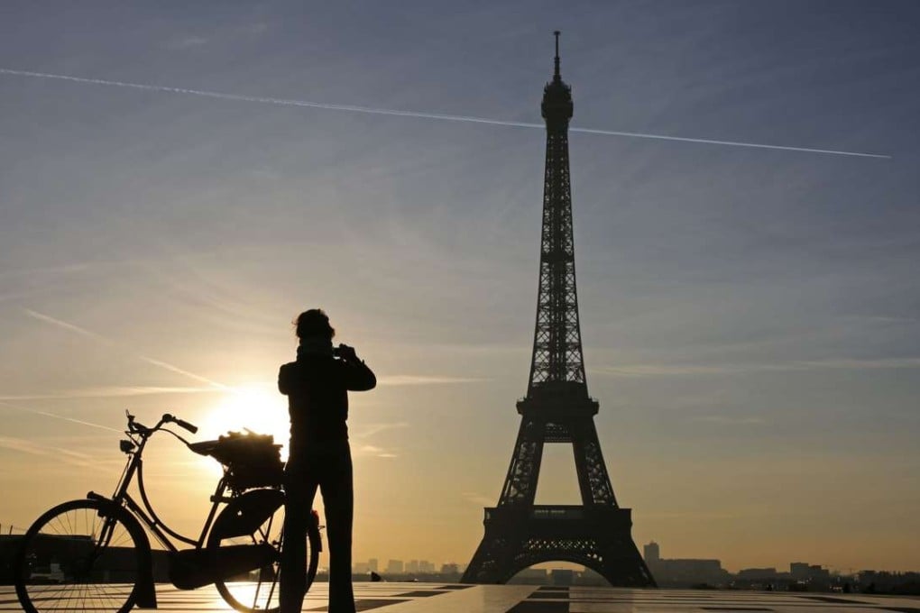 A woman taking a photo from the Trocadero Esplanade in front of the Eiffel Tower at sunrise. Photo: AFP