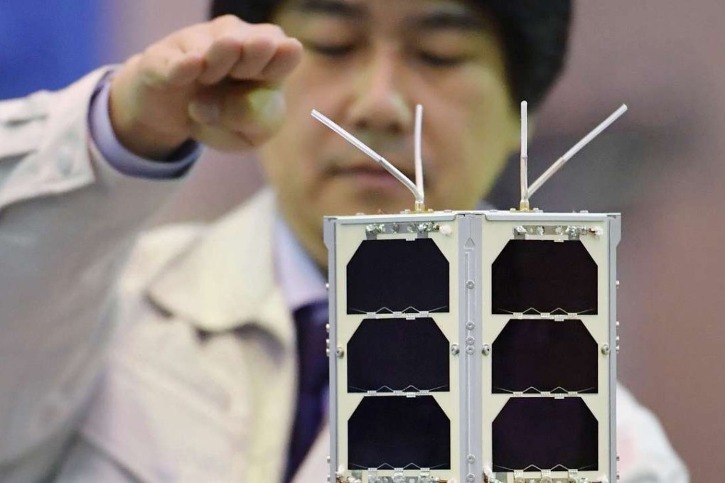 Hiroto Habu, an assistant professor at the Japan Aerospace Exploration Agency, poses with the TRICOM1 ultra small satellite developed by the University of Tokyo, at JAXA's facility in Sagamihara, Kanagawa Prefecture, on Tuesday. The 35cm long satellite is about the size of a loaf of bread. Photo: Kyodo