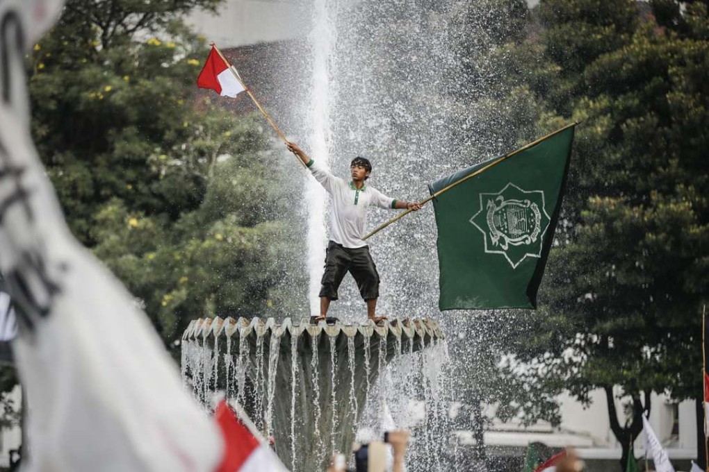 An Indonesian protester waves flags as he stands on a fountain during a protest against allegedly blasphemous remark made by Jakarta's Governor Basuki Tjahaja Purnama. Photo: EPA