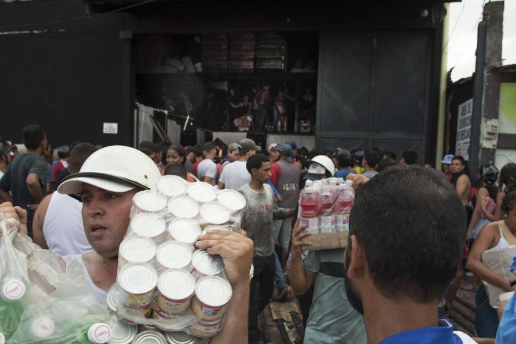 People carry bottles of drinks and cans of sardine as they loot a food warehouse during a protest in La Fria, Tachira, Venezuela. Photo: Bloomberg