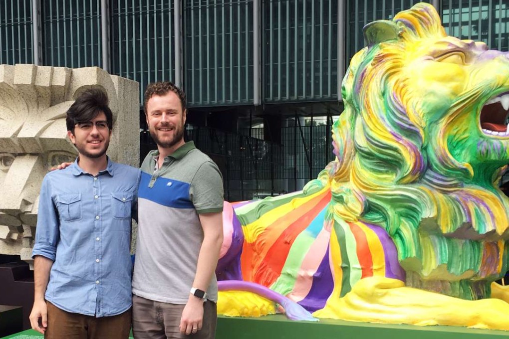 Pedro Lino (left) from Brazil poses with his partner, Adam Dolman of the UK, in front of one of the rainbow lions celebrating “pride and unity” at the HSBC headquarters in Central on December 14. Photo: Kinling Lo