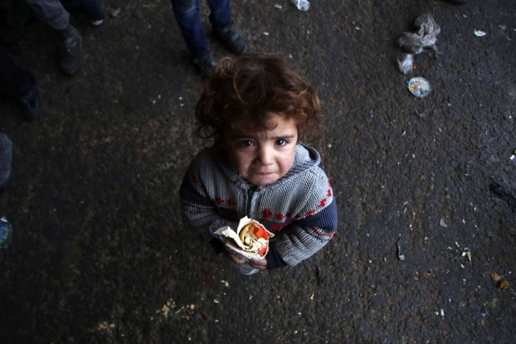 A Syrian child, who fled with his family from rebel-held areas in the city of Aleppo, reacts as he holds a sandwich on December 1, 2016, at a shelter in Jibrin. Picture: AFP